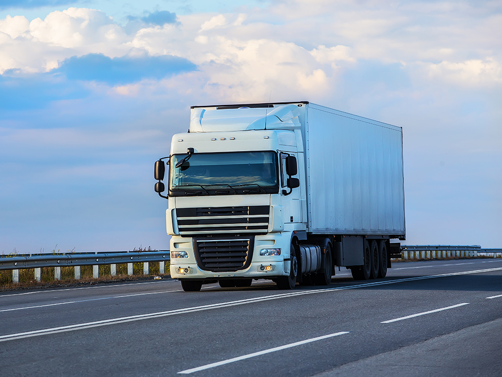 Un camion éclairé par le soleil roule sur une route de campagne